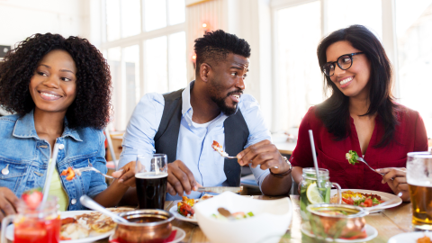 A group sit eating dinner while a couple give each other looks. 