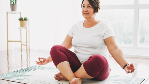 A woman sits on a yoga mat practicing a pose. 